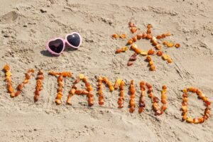 Orange rocks in the sand spelling "Vitamin D" next to pink heart sunglasses